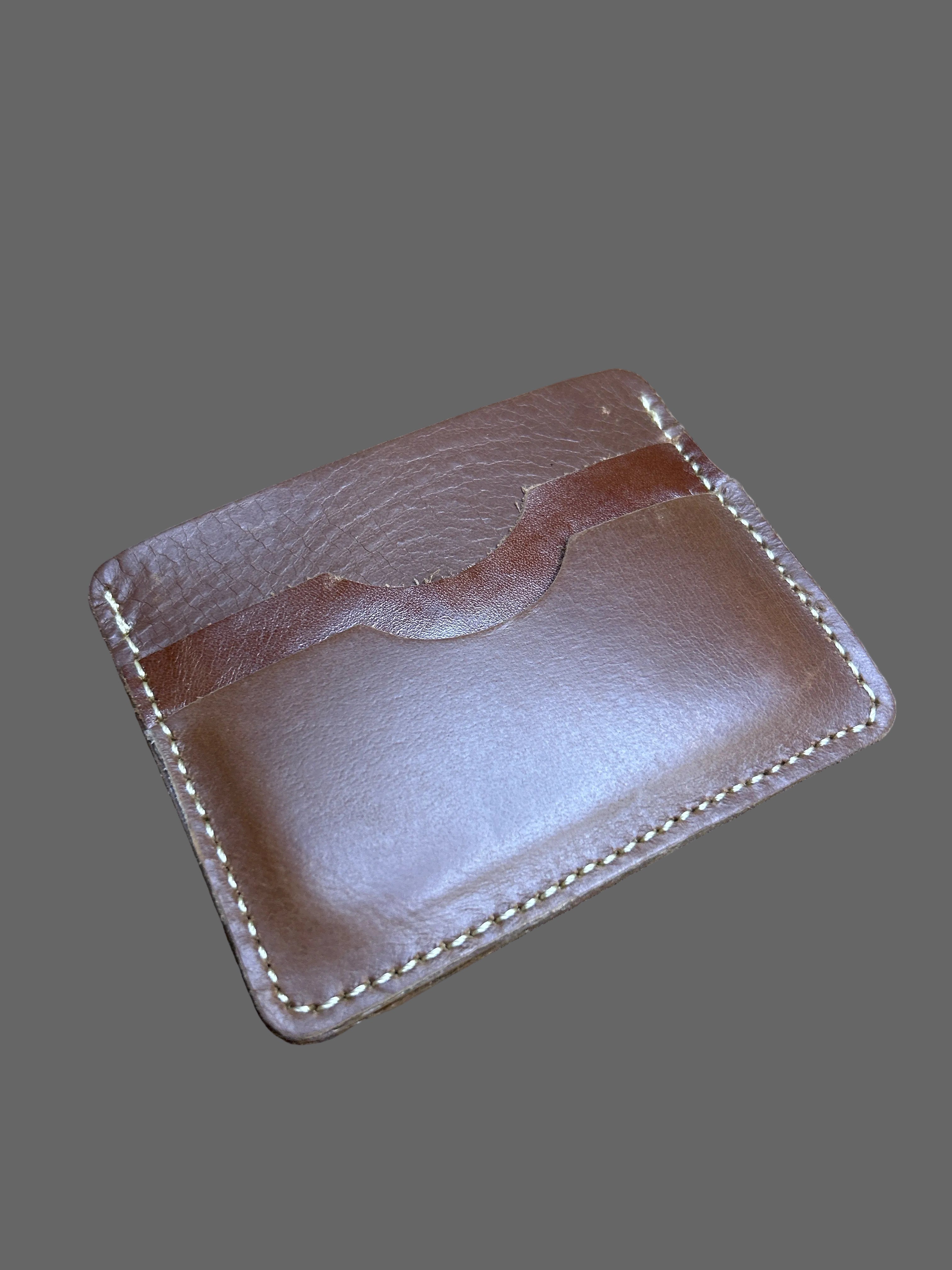 A brown leather card holder wallet with white contrast stitching, resting on a textured brown fur surface.