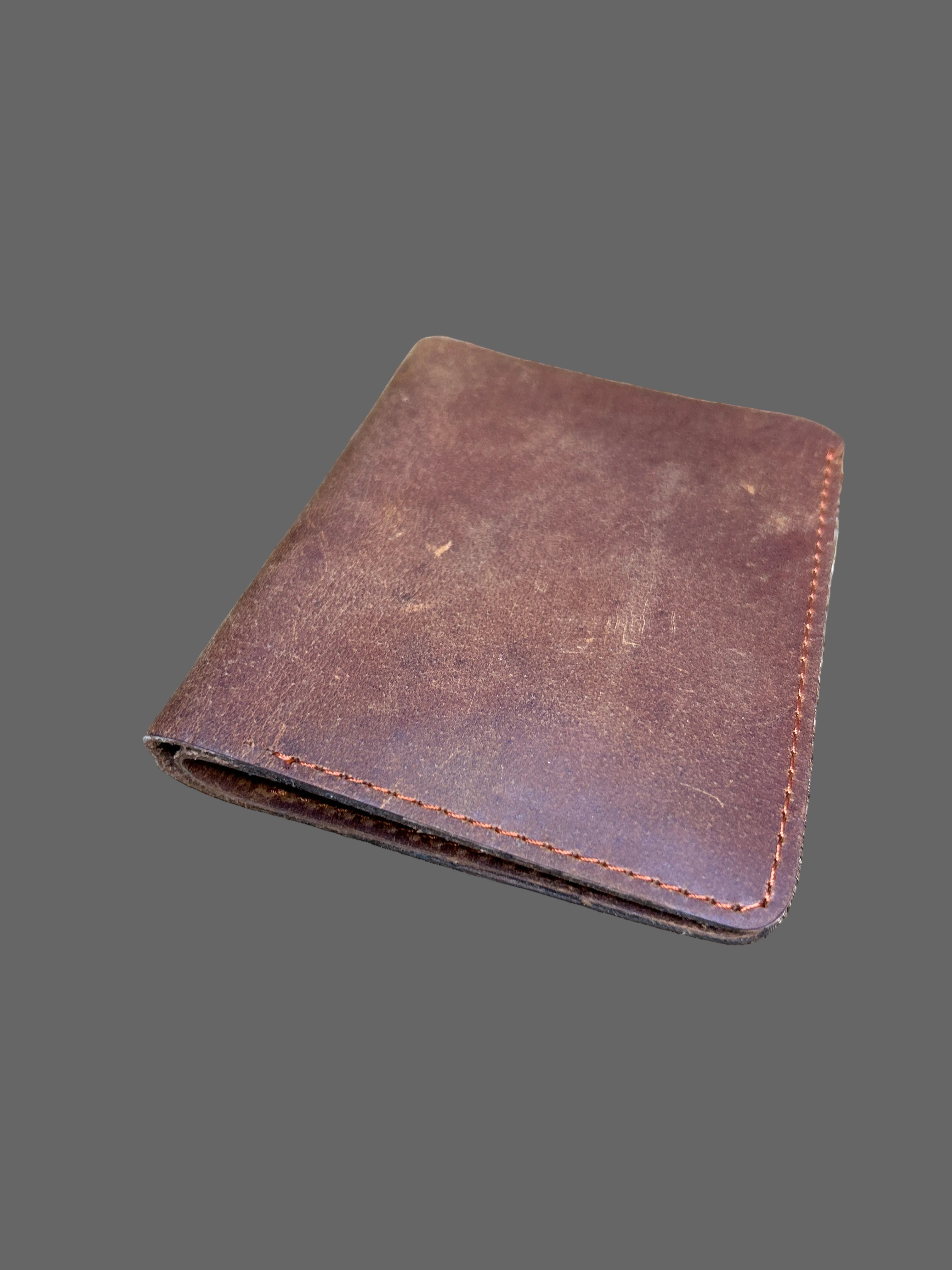 A brown leather bifold wallet with visible stitching, placed on a textured animal fur surface.