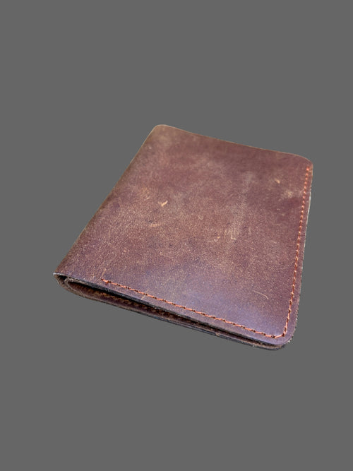 A brown leather bifold wallet with visible stitching, placed on a textured animal fur surface.